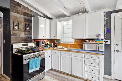Kitchen with white cabinetry, beamed ceiling, light hardwood / wood-style flooring, and oven range.