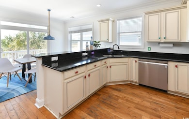 Kitchen with cream cabinetry, hanging light fixtures, crown molding, stainless steel dishwasher, and light wood-style floors