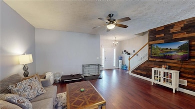 Living room with stairway, ceiling fan, wood finished floors, a textured ceiling, and a chandelier