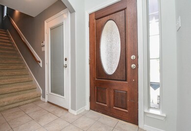 This is the subtle view of the main entrance from the inside, with pale, earth toned tile flooring, neutral walls, and carpeted staircase, left.