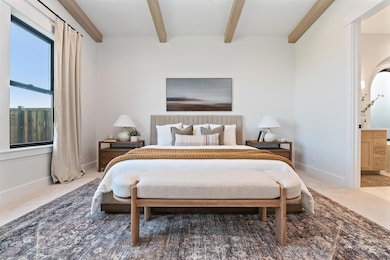 Carpeted bedroom with beam ceiling, connected bathroom, and arched walkways