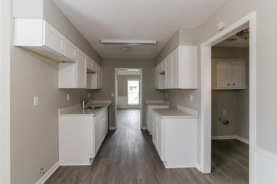 Kitchen with a textured ceiling, dark wood-style flooring, white cabinetry, and light countertops