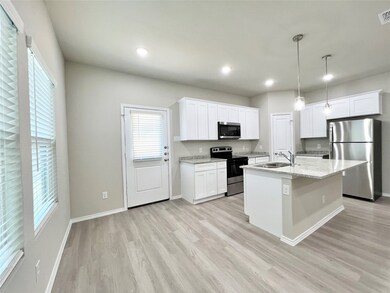 Kitchen with stainless steel appliances, white cabinetry, a kitchen island with sink, pendant lighting, and light wood-type flooring