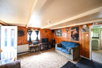 Carpeted living room with beam ceiling, a textured ceiling, and wood walls