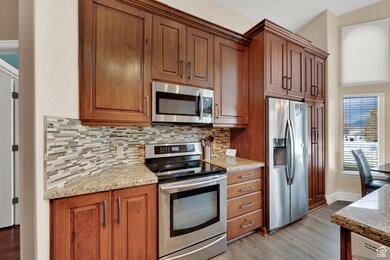 Kitchen featuring appliances with stainless steel finishes, decorative backsplash, light stone counters, and light wood-style flooring
