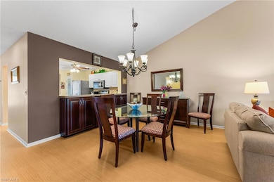 Dining space with high vaulted ceiling, light wood finished floors, baseboards, and ceiling fan with notable chandelier
