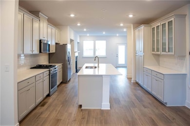 Kitchen with decorative backsplash, stainless steel appliances, a center island with sink, light wood-style flooring, and recessed lighting