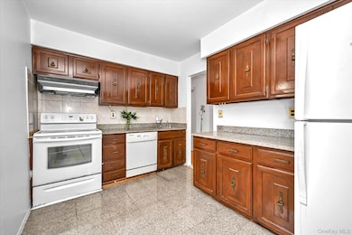Kitchen featuring white appliances, granite floors, under cabinet range hood, backsplash, and light stone counters