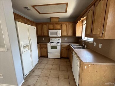 Kitchen featuring white appliances, light countertops, light tile patterned flooring, and brown cabinetry