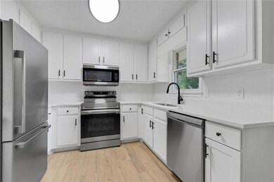 Kitchen featuring appliances with stainless steel finishes, a sink, light countertops, tasteful backsplash, and white cabinetry