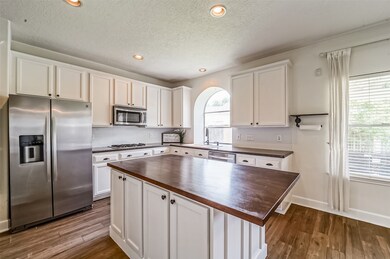 The island kitchen is anchored by a large butcher block island with space for two barstools. Other fine finishes include dark granite countertops, a micro subway tile backsplash, creamy white cabinetry, and recessed lighting.