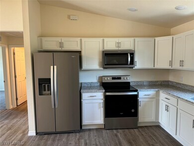Kitchen with white cabinetry, appliances with stainless steel finishes, light stone counters, wood-type flooring, and vaulted ceiling