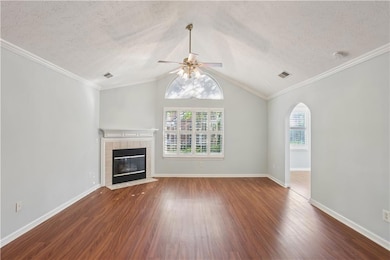 Unfurnished living room with wood finished floors, ceiling fan, a tiled fireplace, arched walkways, and a textured ceiling