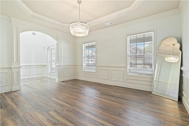 Unfurnished dining area with a raised ceiling, healthy amount of natural light, wood finished floors, a chandelier, and ornamental molding