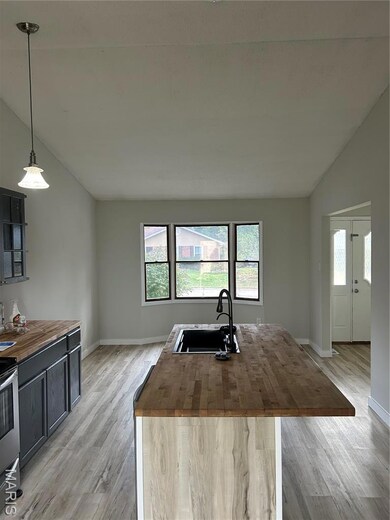 Kitchen with butcher block countertops, vaulted ceiling, light wood-style flooring, a center island with sink, and hanging light fixtures