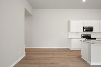 Kitchen with stainless steel appliances, tasteful backsplash, light wood-style flooring, white cabinetry, and light stone countertops