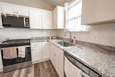 Kitchen with appliances with stainless steel finishes, light stone counters, white cabinets, tasteful backsplash, and light wood-style flooring