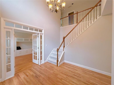 Entryway with french doors, stairway, light wood finished floors, a chandelier, and baseboards