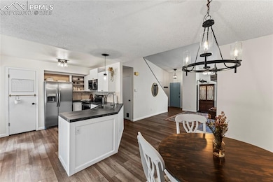 Kitchen with stainless steel appliances, dark countertops, open shelves, a chandelier, and dark wood finished floors