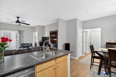 Kitchen with light brown cabinetry, light wood finished floors, stainless steel dishwasher, dark countertops, and ceiling fan