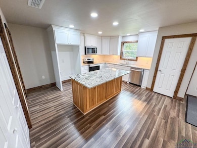 Kitchen featuring dark wood-style floors, appliances with stainless steel finishes, white cabinetry, recessed lighting, and light stone countertops