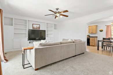 Living area with a ceiling fan, ornamental molding, light carpet, arched walkways, and built in features
