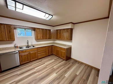 Kitchen featuring stainless steel dishwasher, light countertops, light wood finished floors, ornamental molding, and brown cabinetry