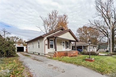 Bungalow-style home featuring a front lawn, covered porch, a chimney, a garage, and an outbuilding