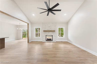 Unfurnished living room with high vaulted ceiling, a chandelier, light wood-style floors, a stone fireplace, and recessed lighting