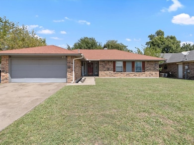 Single story home featuring a front lawn, roof with shingles, driveway, brick siding, and a garage