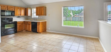 Kitchen featuring black appliances, plenty of natural light, vaulted ceiling, and light tile patterned floors