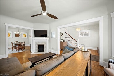 Living room featuring dark wood-type flooring, a stone fireplace, and ceiling fan with notable chandelier