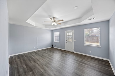 Spare room featuring a tray ceiling, healthy amount of natural light, dark wood finished floors, and ceiling fan