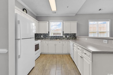 Kitchen with white appliances, a peninsula, light wood-style floors, backsplash, and ornamental molding