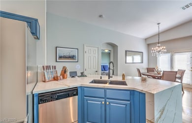 Kitchen featuring blue cabinetry, light stone counters, dishwasher, and lofted ceiling