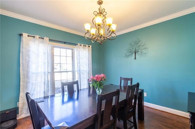 Dining area with wood finished floors, a notable chandelier, ornamental molding, and baseboards