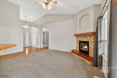Unfurnished living room with vaulted ceiling, carpet, a glass covered fireplace, arched walkways, and ceiling fan