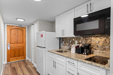 Kitchen featuring white cabinetry, black appliances, tasteful backsplash, and dark wood-type flooring