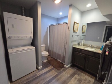 Bathroom featuring dark wood-style floors, vanity, stacked washer / drying machine, and recessed lighting