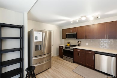 Kitchen featuring appliances with stainless steel finishes, decorative backsplash, light countertops, light wood-style floors, and dark brown cabinetry