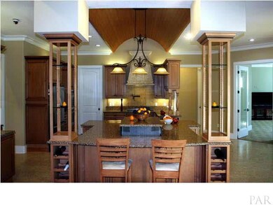 View of kitchen from great room. Granite countertops w/chiseled edge, barrel tongue & groove ceiling, built-in wine rack & display shelves. Family/media room to your right.