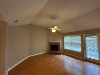 Unfurnished living room featuring lofted ceiling, a ceiling fan, wood finished floors, a textured ceiling, and a brick fireplace