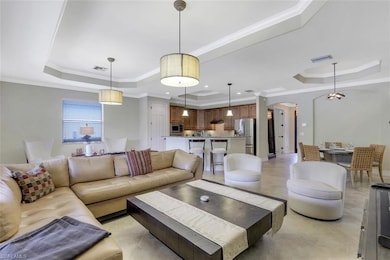 Living room featuring a raised ceiling, ornate columns, crown molding, and arched walkways
