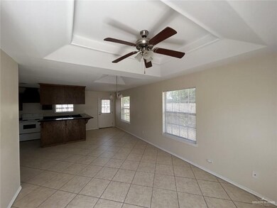 Unfurnished living room featuring a raised ceiling, light tile patterned floors, a ceiling fan, and baseboards