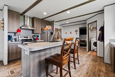 Kitchen with wall chimney range hood, wood finished floors, a kitchen bar, stainless steel appliances, and recessed lighting