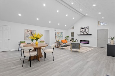 Dining space featuring beamed ceiling, high vaulted ceiling, light wood-style flooring, a glass covered fireplace, and recessed lighting