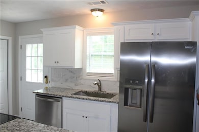 Kitchen with stainless steel appliances, a sink, stone counters, white cabinetry, and tasteful backsplash