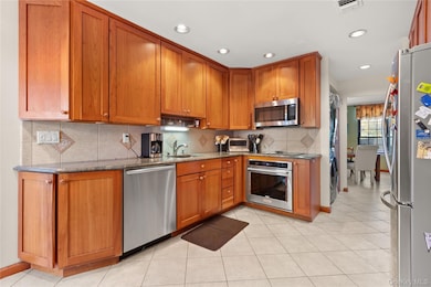 Kitchen featuring brown cabinets, dark stone countertops, backsplash, appliances with stainless steel finishes, and recessed lighting