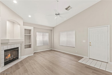 Unfurnished living room featuring built in features, wood finished floors, a tiled fireplace, a ceiling fan, and high vaulted ceiling