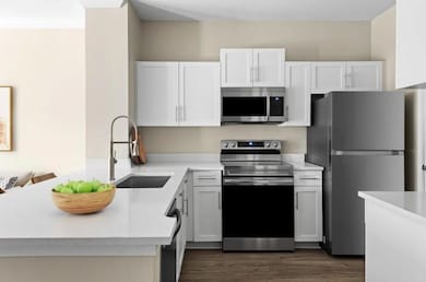 Kitchen featuring a sink, stainless steel appliances, light countertops, a peninsula, and dark wood-type flooring